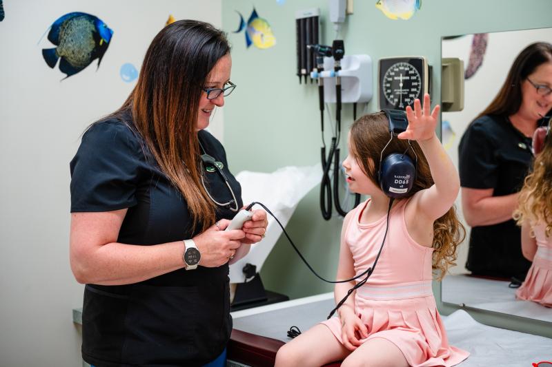 a girl wearing headphones raising her left arm while a medical provider helps